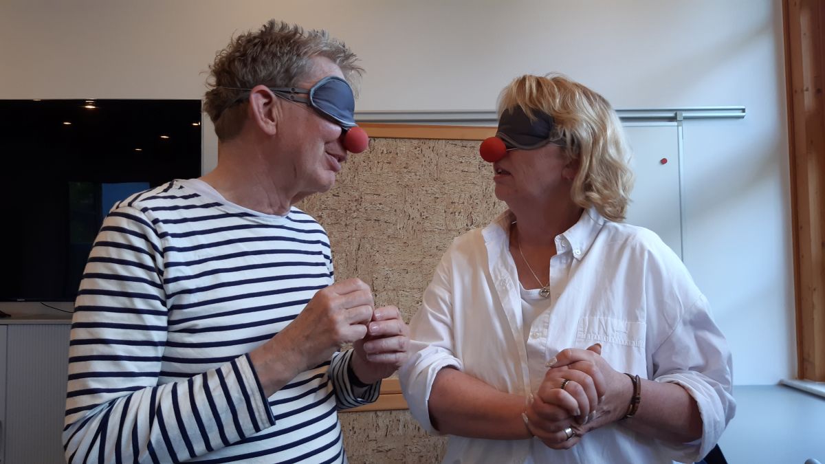 Ein Mann im gestreiften Shirt und eine Frau in weißer Bluse stehen beieinander und reden miteinander. Beide tragen eine rote Nase.